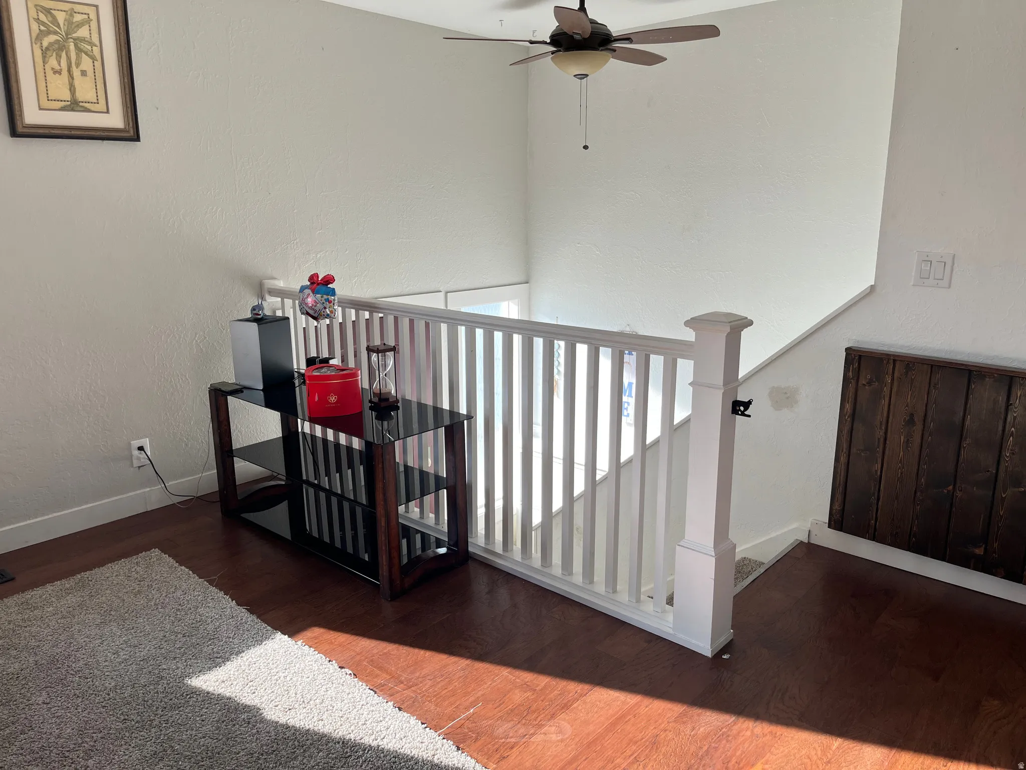 Stairs with wood finished floors, a ceiling fan, and a textured wall