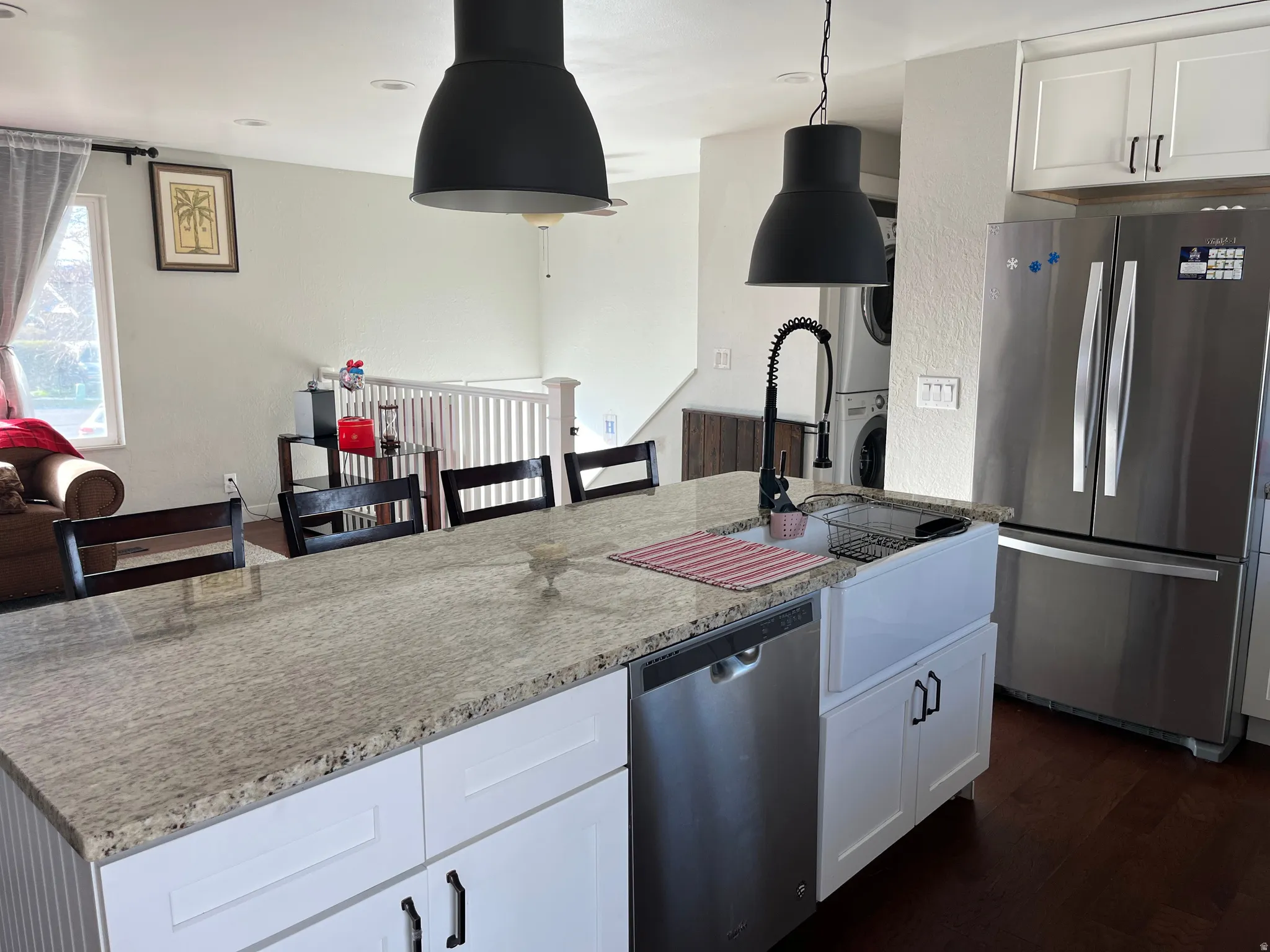 Kitchen featuring white cabinets, stainless steel appliances, light stone countertops, a kitchen island with sink, and stacked washing machine and dryer