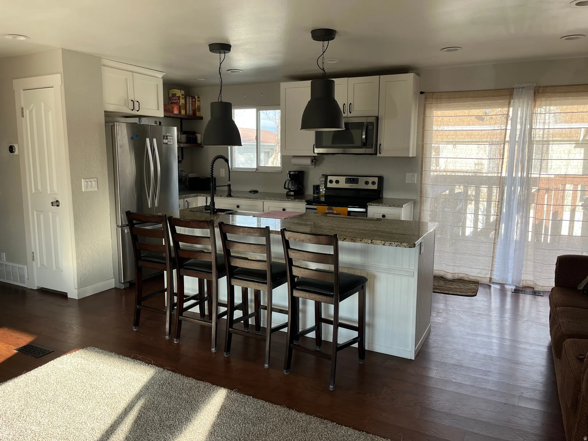 Kitchen with a breakfast bar area, white cabinetry, stainless steel appliances, dark wood-style floors, and pendant lighting