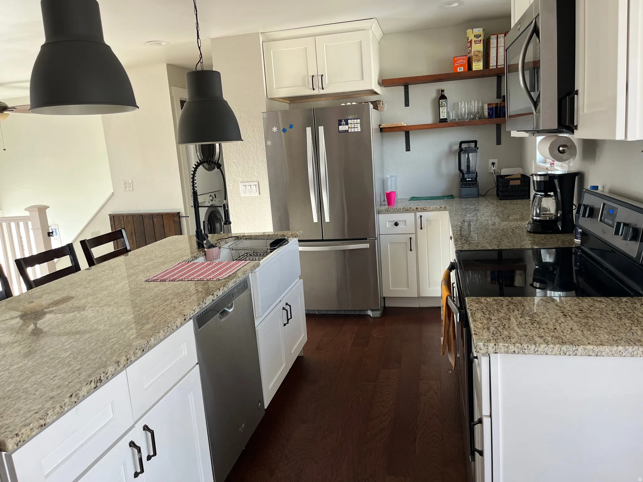 Kitchen featuring stainless steel appliances, white cabinets, light stone countertops, and a center island with sink