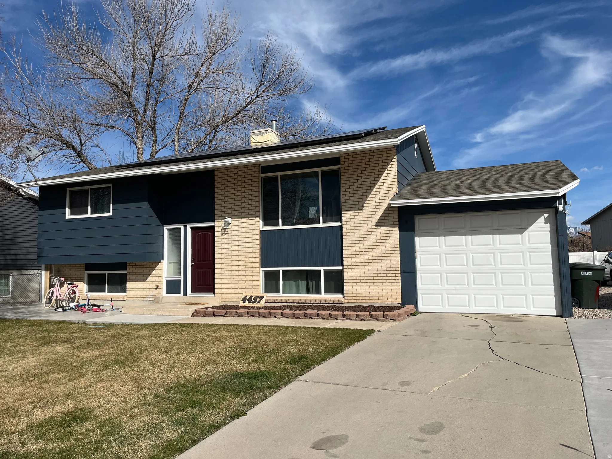 Raised ranch featuring an attached garage, a chimney, driveway, a front yard, and brick siding