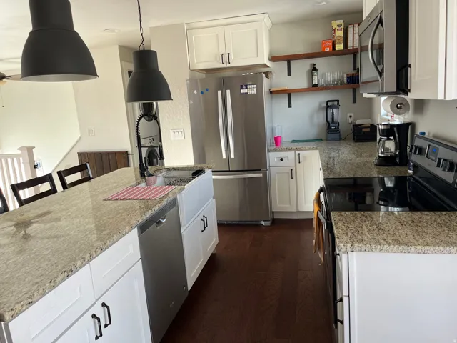 Kitchen featuring stainless steel appliances, white cabinets, light stone countertops, and a center island with sink