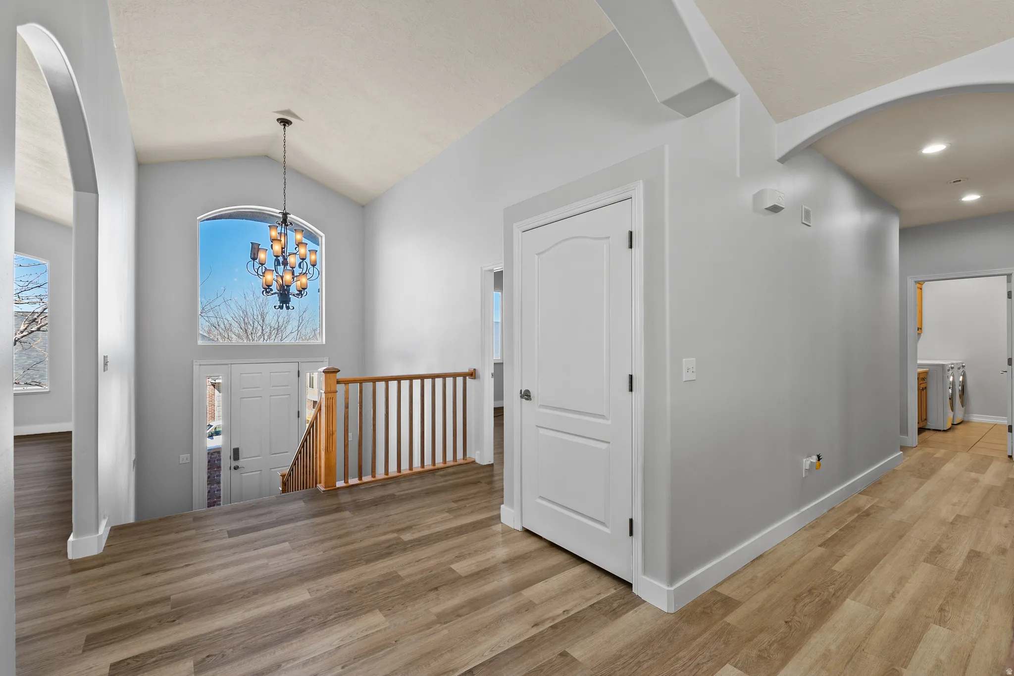 Entrance foyer featuring arched walkways, light wood-type flooring, vaulted ceiling, and a chandelier.