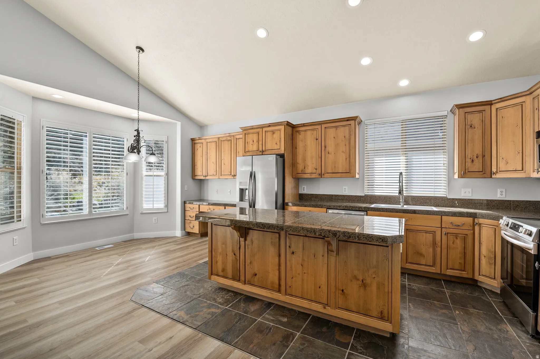 Kitchen with tile counters, stainless steel appliances, wood finish cabinetry, vaulted ceiling, and a kitchen island