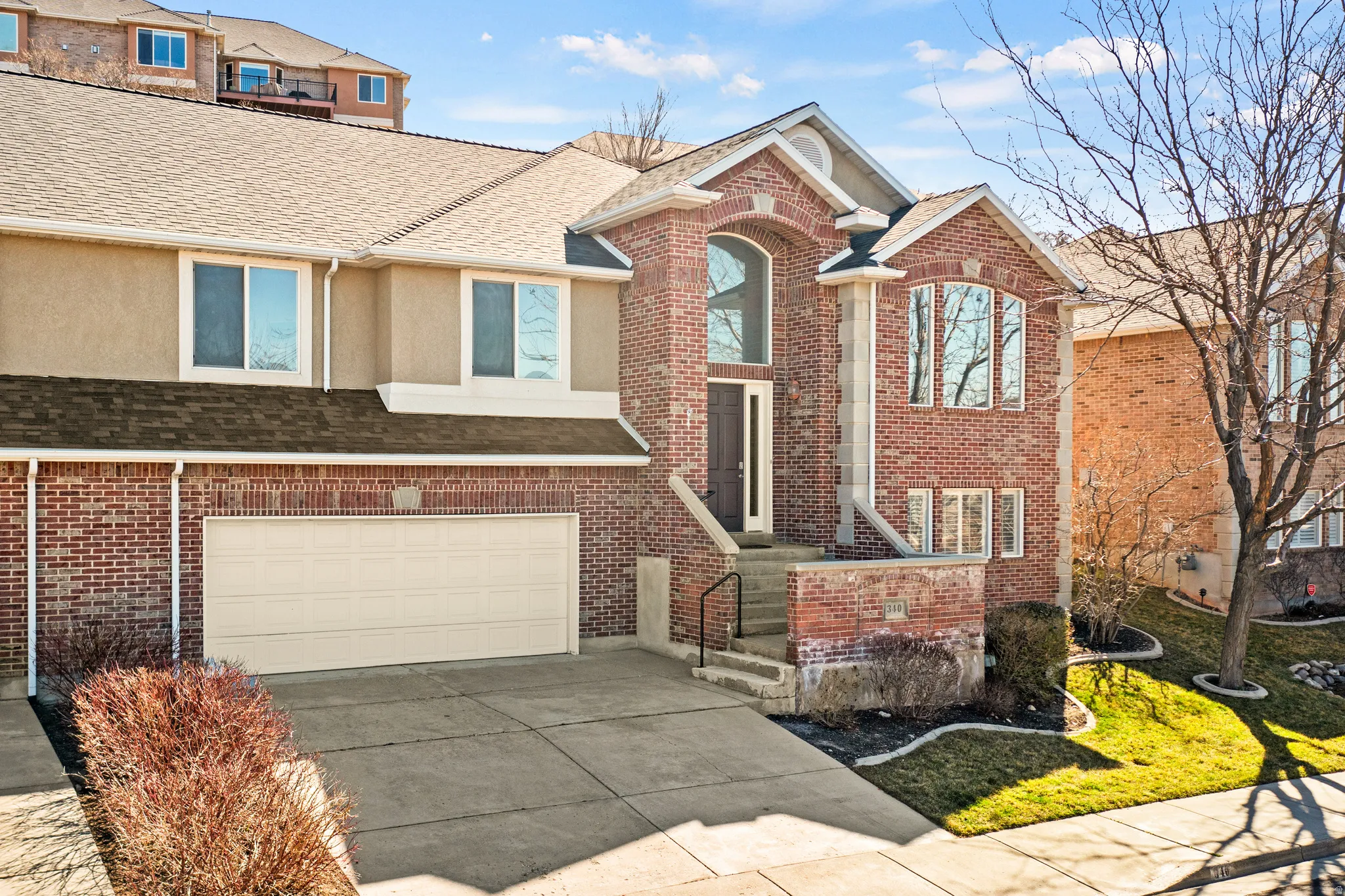 View of front of house featuring roof with shingles, driveway, an attached garage, brick siding, and stucco siding
