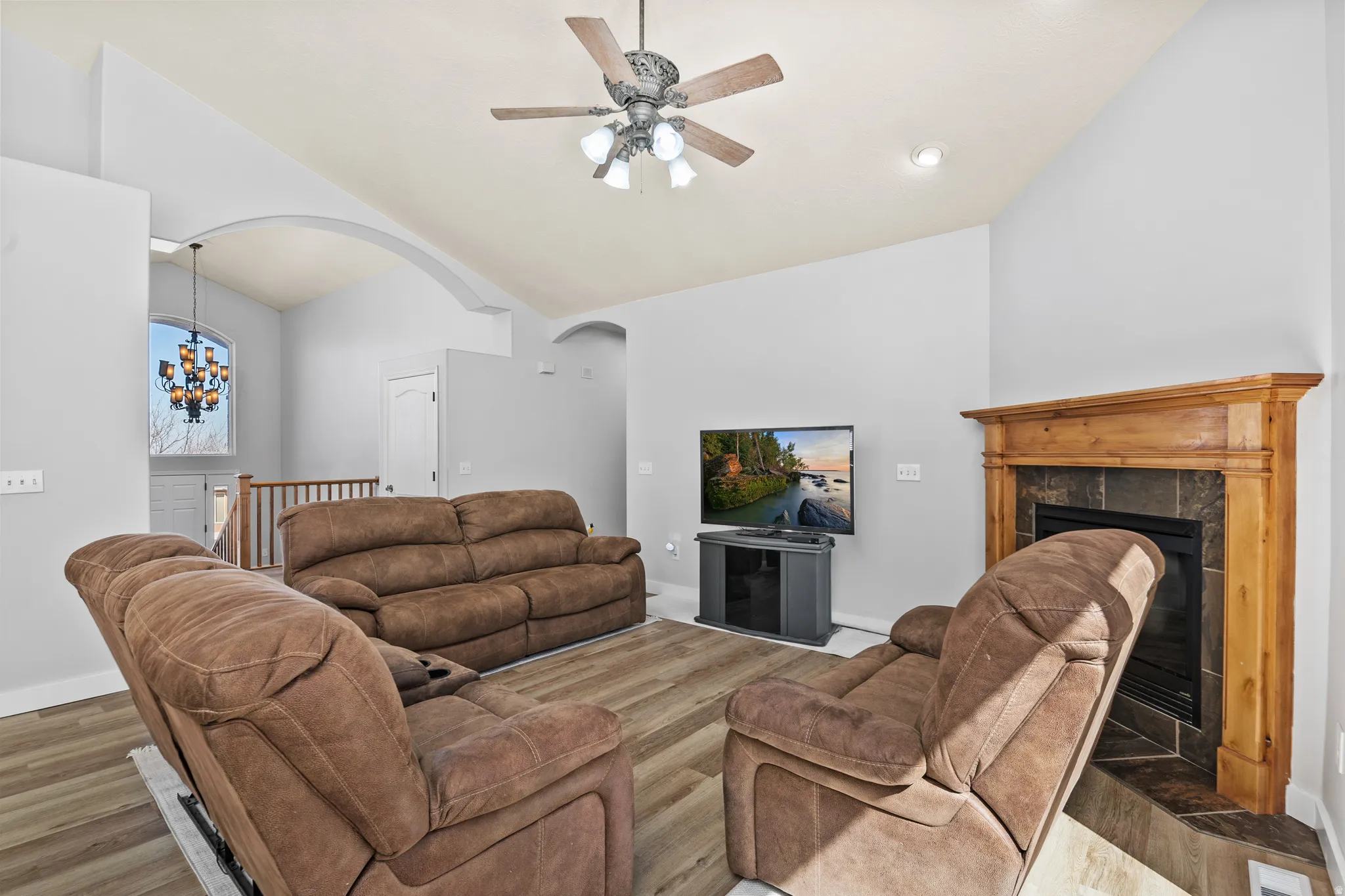 Living room with ceiling fan, wood finished floors, fireplace, suspended lighting, and lofted ceiling