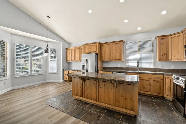 Kitchen with tile counters, stainless steel appliances, wood finish cabinetry, vaulted ceiling, and a kitchen island
