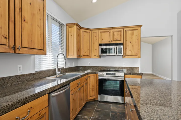 Kitchen with tile counters, stainless steel appliances, lofted ceiling, recessed lighting, and wood finish cabinetry