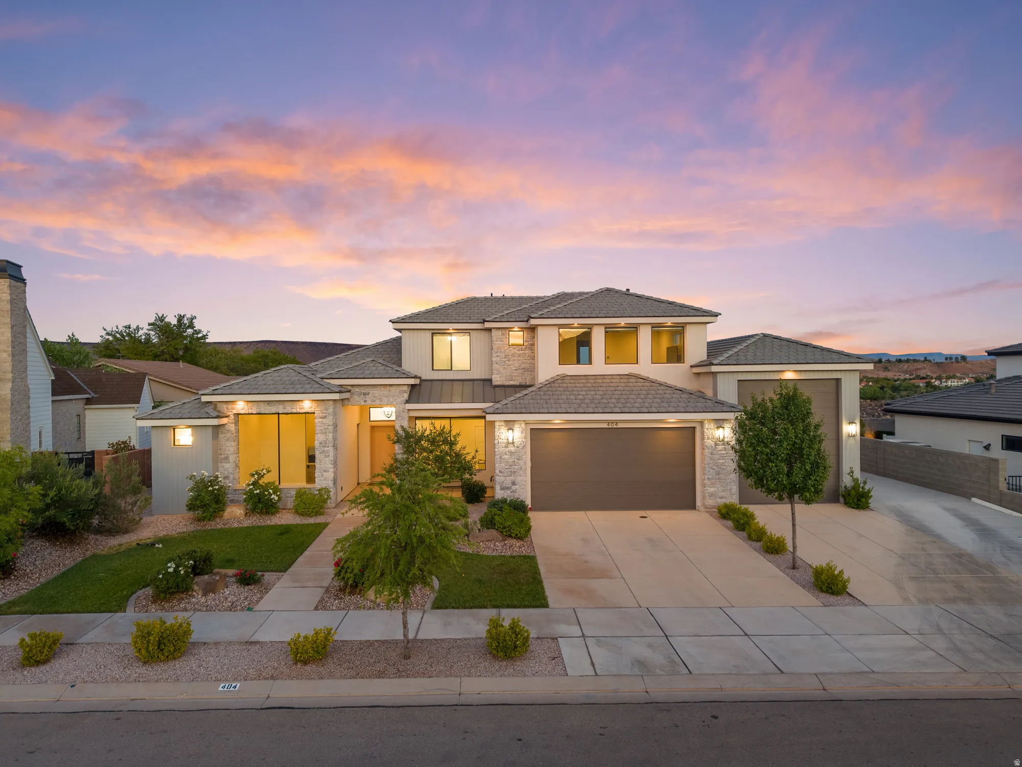 Stone and stucco exterior featuring a multi-car driveway, attached garage, and a manicured lawn with mature landscaping