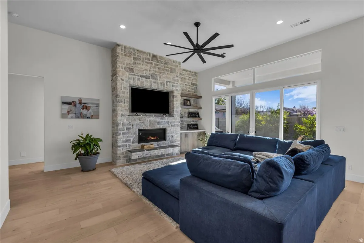 Living room featuring light wood finished floors, ceiling fan, a stone fireplace, and recessed lighting