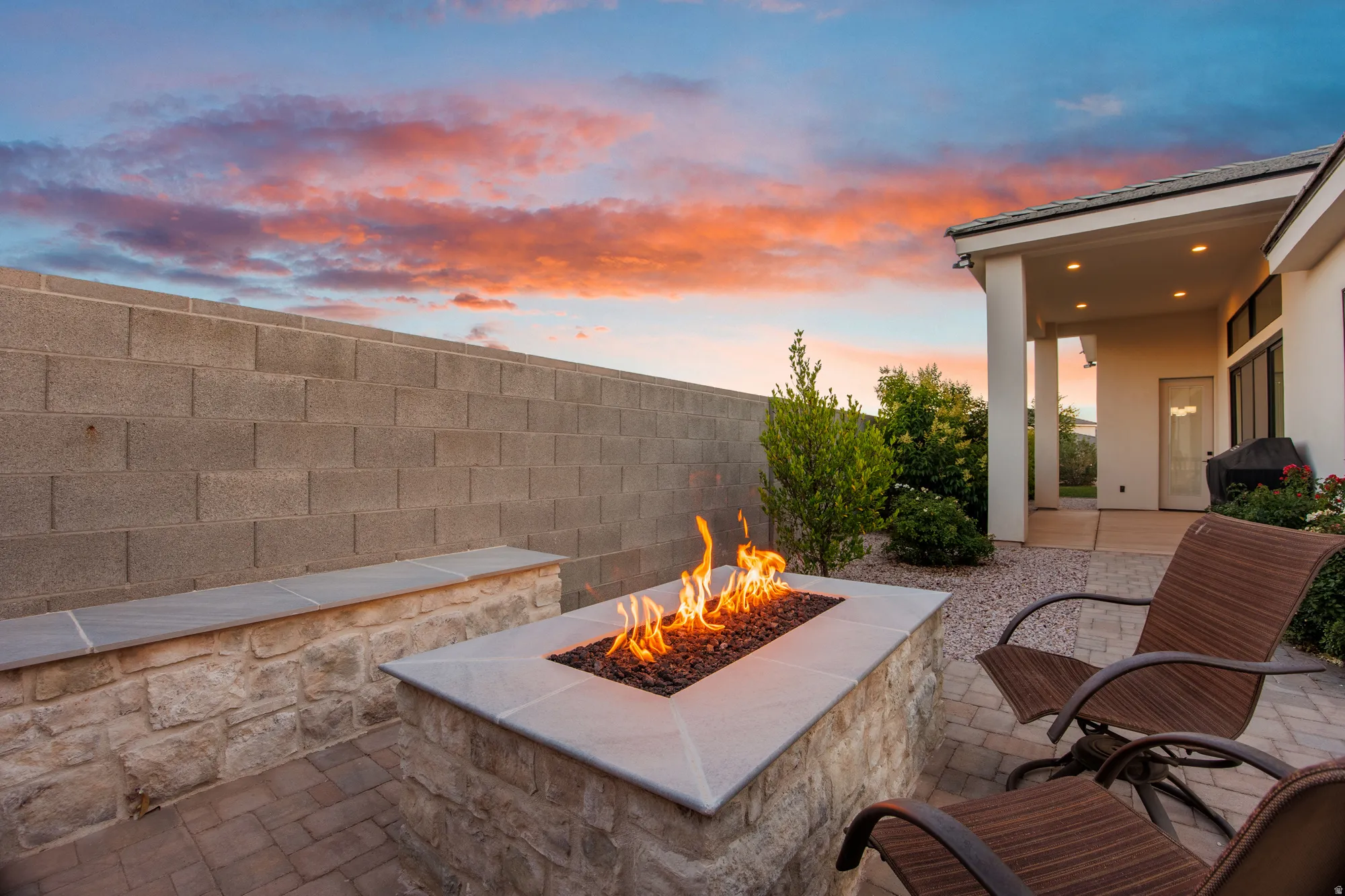 Outdoor patio featuring a built-in fire pit with a stone base and light-colored capping, accompanied by a matching low stone wall with a cap