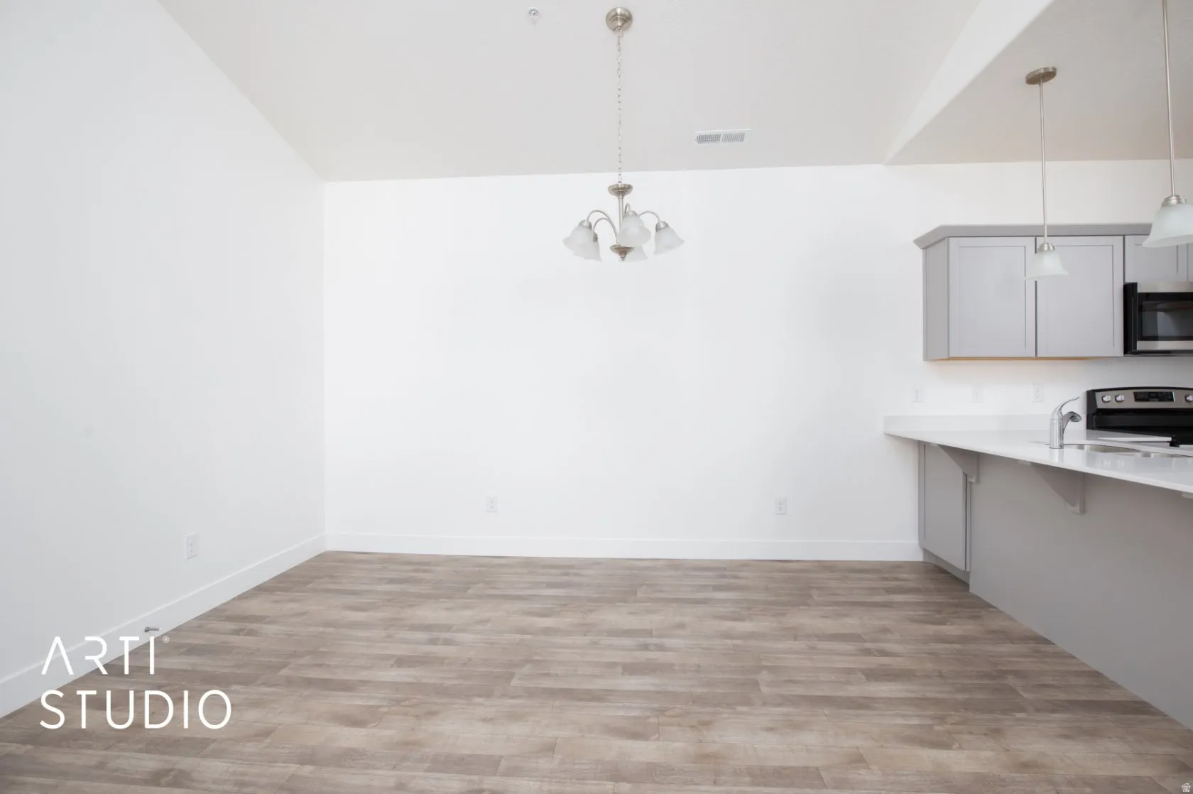 Unfurnished dining area featuring light wood-style flooring, hanging lights, and vaulted ceiling