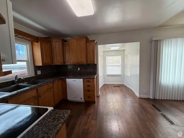 Kitchen with wood finish cabinets, electric cooktop, white dishwasher, dark wood finished floors, and plenty of natural light