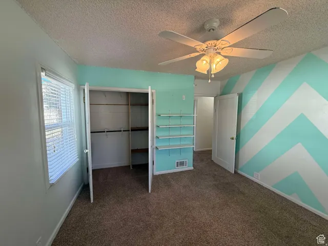 Unfurnished bedroom with dark carpet, ceiling fan, a closet, a textured ceiling, and an accent wall