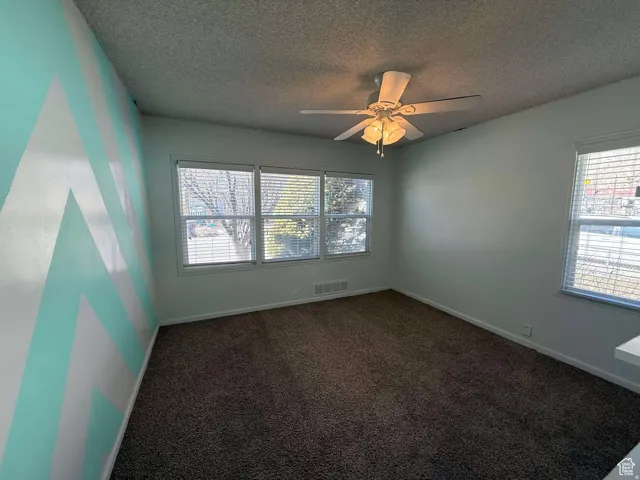 Empty room featuring dark carpet, a ceiling fan, and a textured ceiling