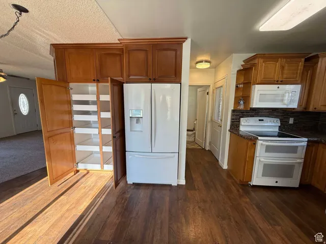Kitchen featuring white appliances, wood finish cabinets, tasteful backsplash, dark wood finished floors, and a textured ceiling