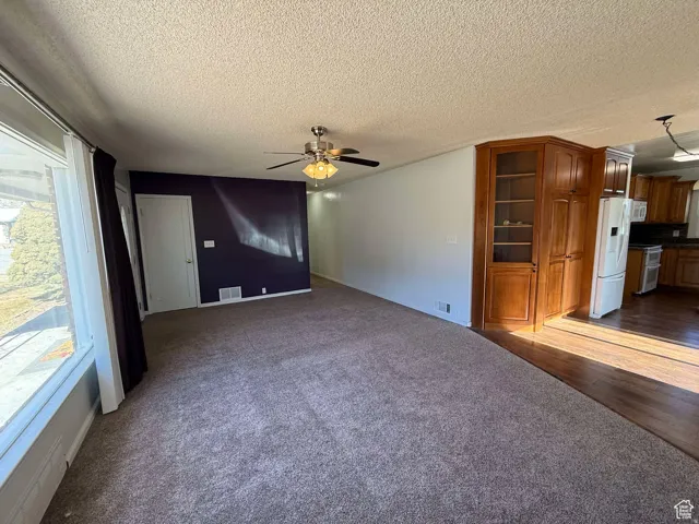 Unfurnished living room with ceiling fan, dark colored carpet, and a textured ceiling