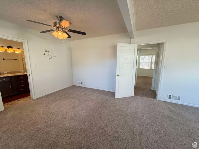 Unfurnished bedroom with dark carpet, a textured ceiling, ensuite bathroom, a ceiling fan, and beamed ceiling