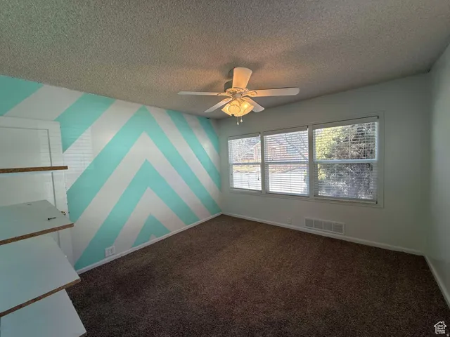 Unfurnished room featuring wallpapered walls, dark carpet, ceiling fan, a textured ceiling, and an accent wall