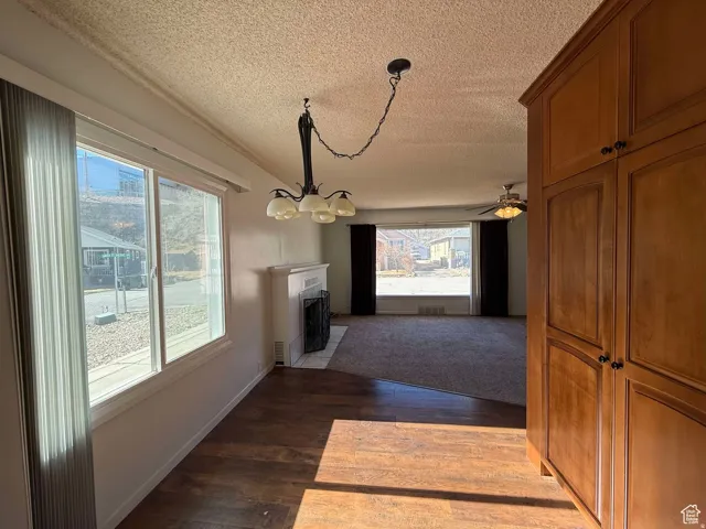 Unfurnished dining area with dark wood-type flooring, a fireplace with flush hearth, a textured ceiling, hanging lights, and ceiling fan