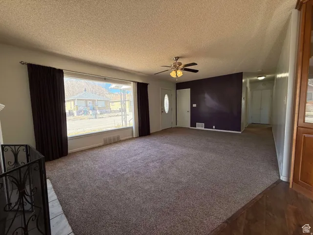Unfurnished living room with a ceiling fan, carpet, and a textured ceiling