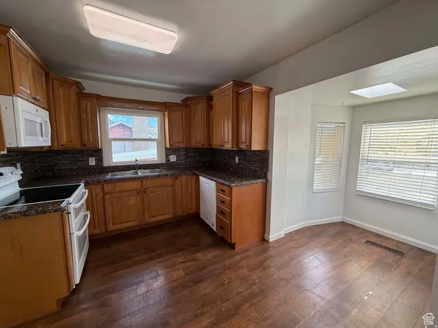 Kitchen with white appliances, wood finish cabinetry, dark wood-style flooring, and decorative backsplash