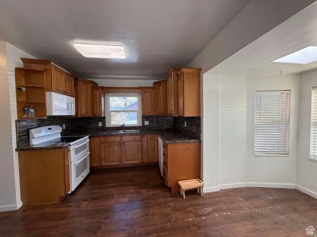 Kitchen with wood finish cabinetry, white appliances, dark wood finished floors, open shelves, and dark stone countertops