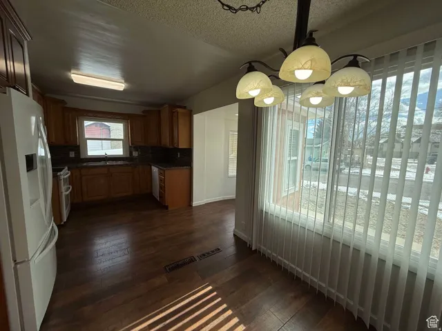 Kitchen featuring white refrigerator with ice dispenser, dark wood-type flooring, range with two ovens, wood finish cabinetry, and a textured ceiling