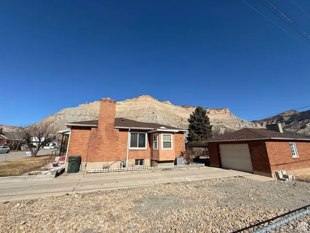 View of front of house featuring a mountain view, a chimney, an outbuilding, brick siding, and concrete driveway