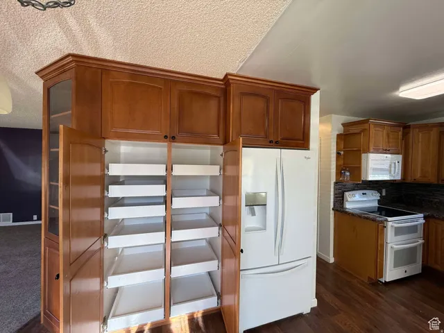 Kitchen featuring white appliances, wood finish cabinetry, backsplash, a textured ceiling, and dark wood finished floors