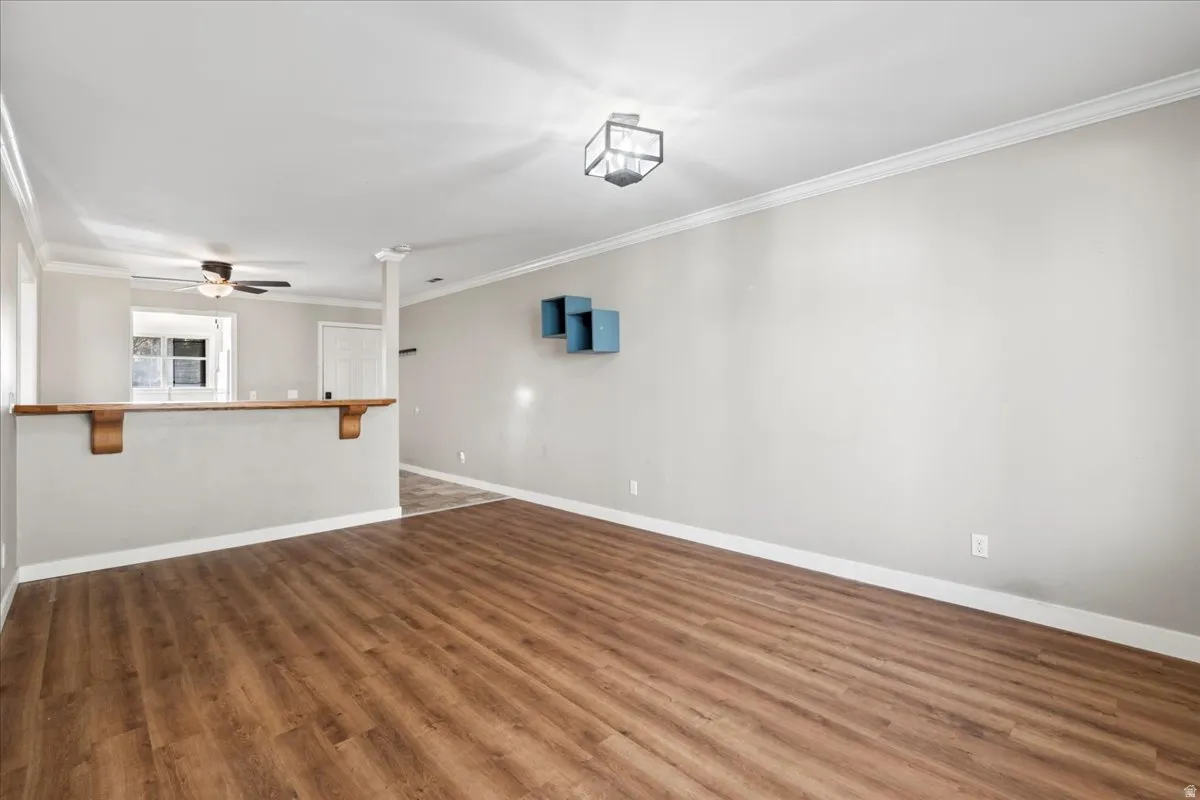 Empty room with crown molding, dark wood-style floors, and a ceiling fan