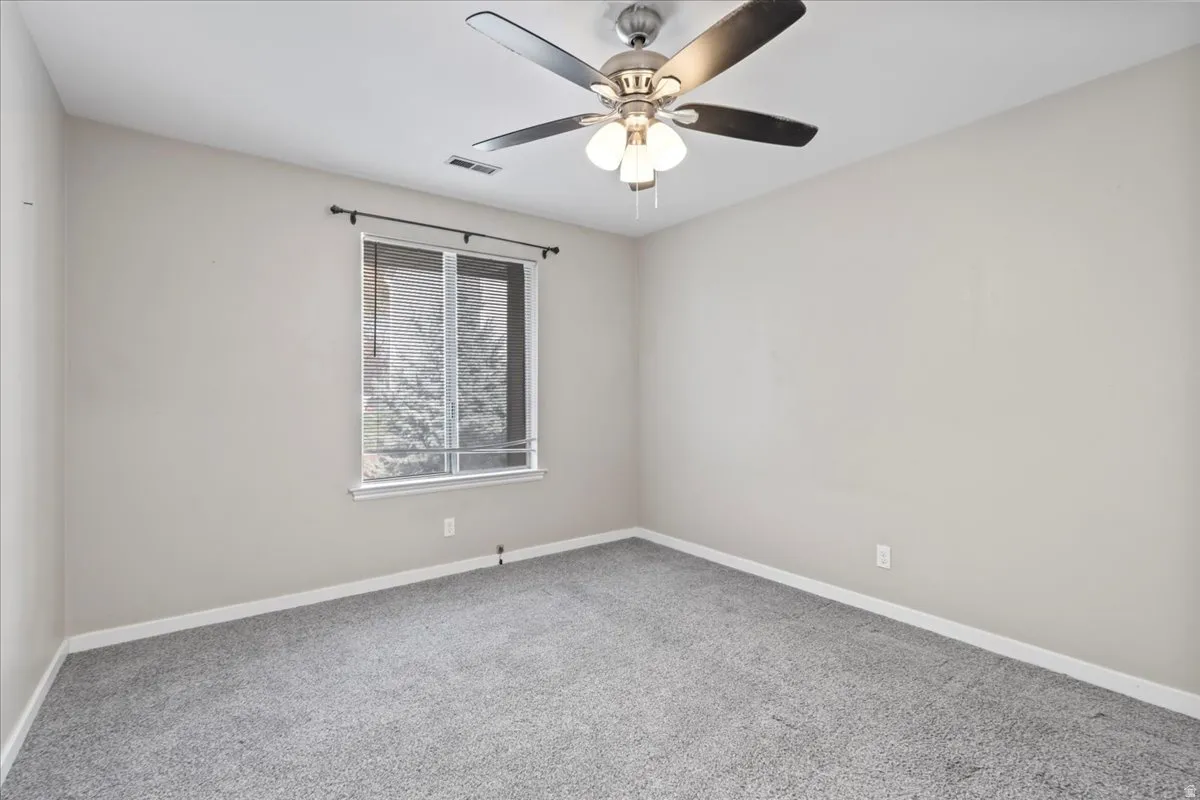 Carpeted empty room with baseboards and a ceiling fan