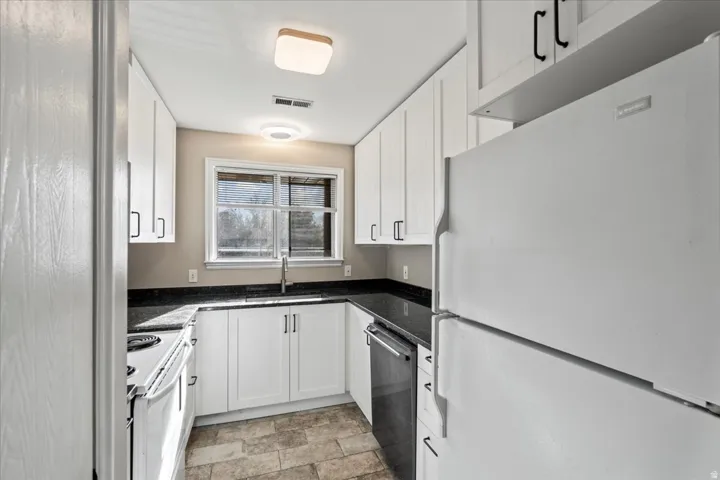 Kitchen featuring white appliances, white cabinets, and dark stone countertops