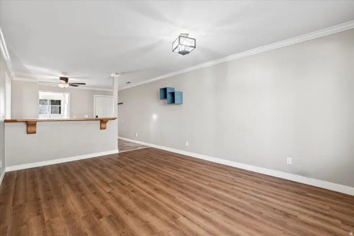 Empty room with crown molding, dark wood-style floors, and a ceiling fan