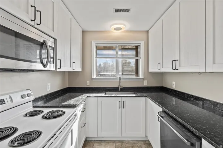 Kitchen featuring stainless steel appliances, white cabinets, and dark stone counters