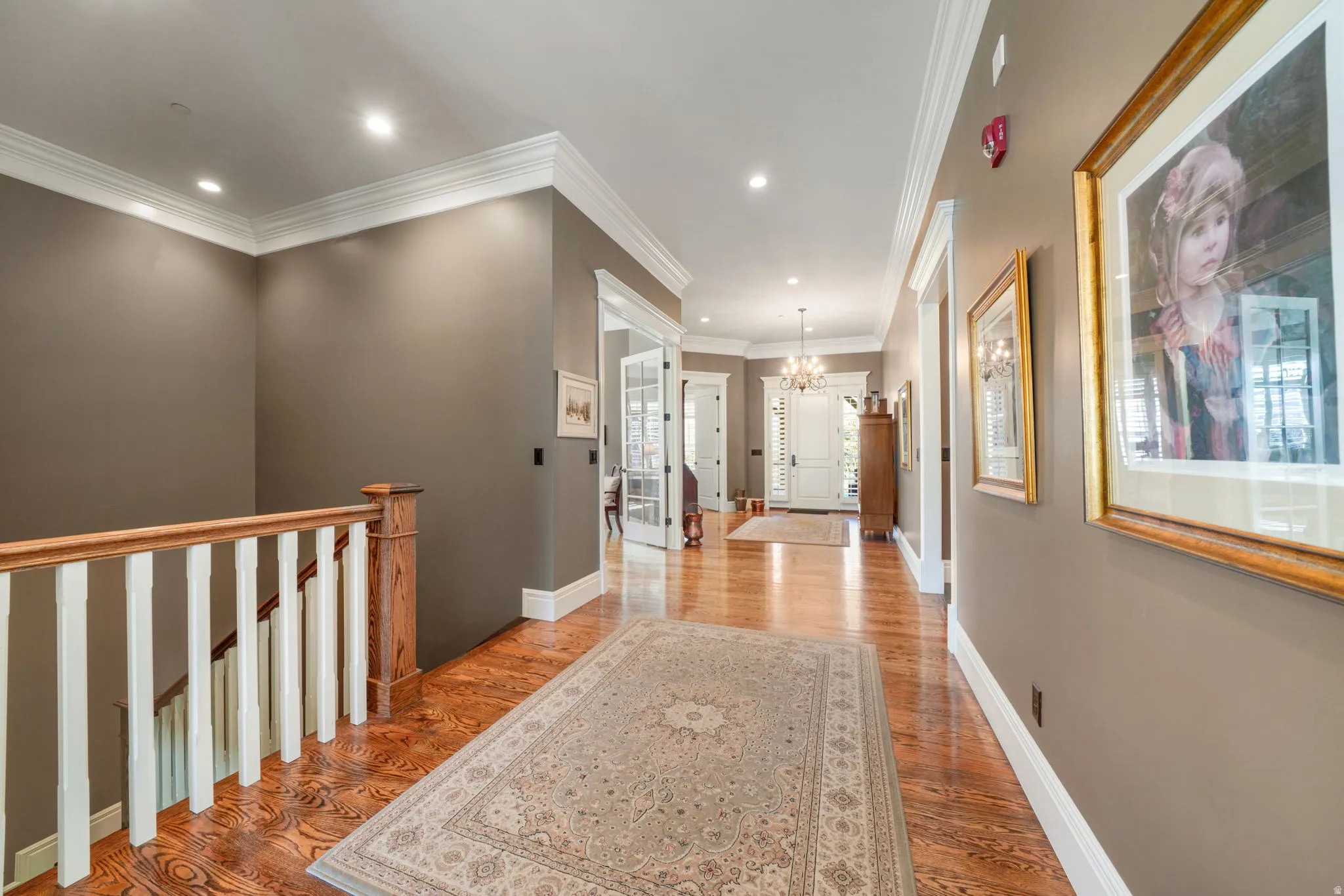 Hall with light wood-style flooring, an upstairs landing, hanging lights, and ornamental molding