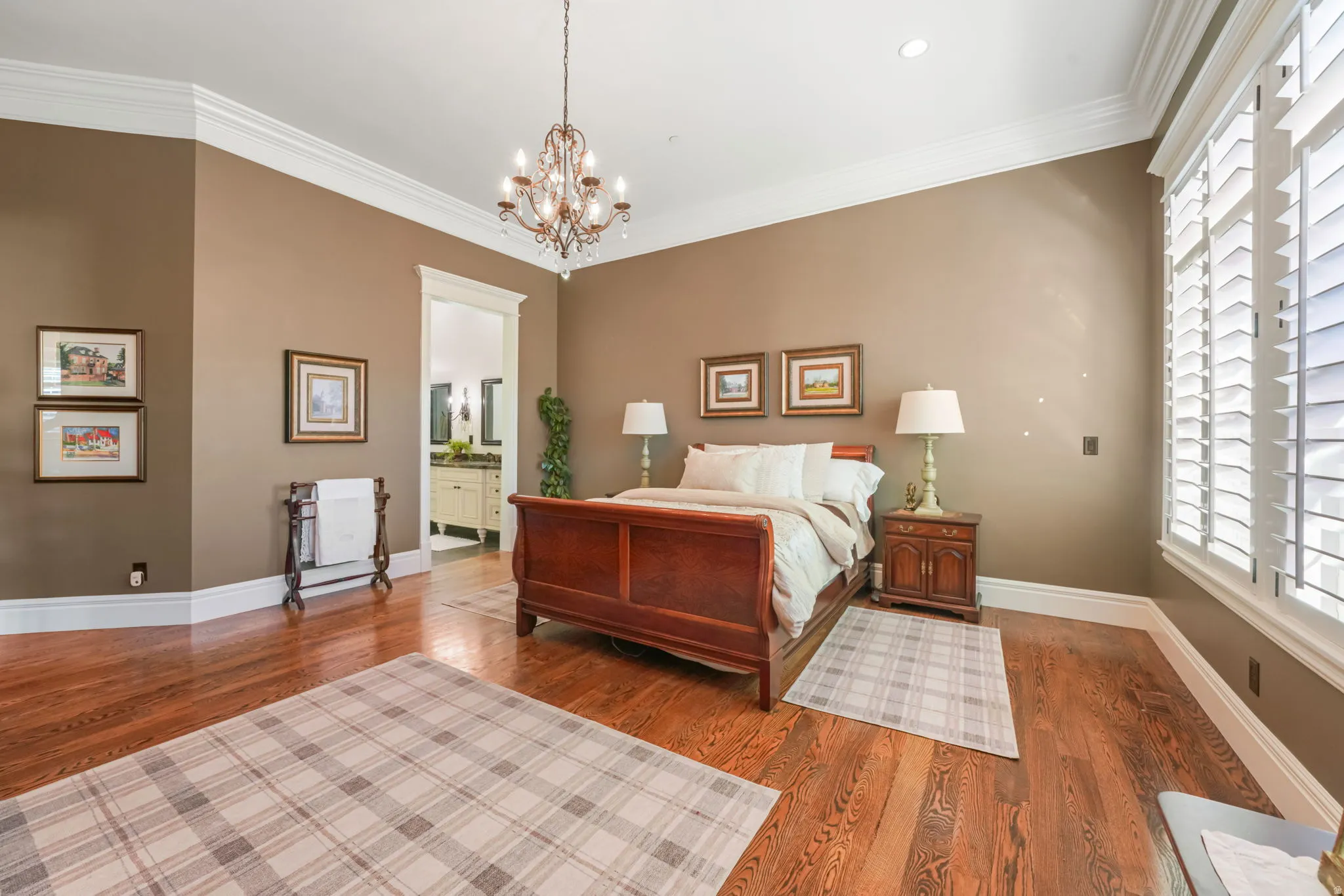 Bedroom featuring dark wood-style floors, ornamental molding, suspended lighting, and connected bathroom