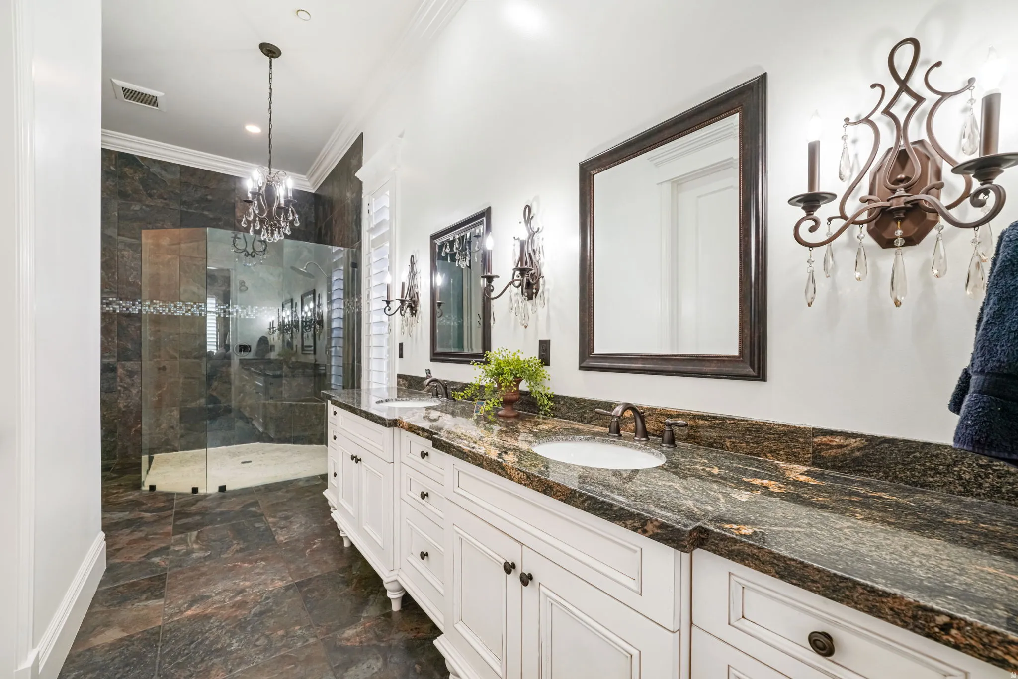 Bathroom with ornamental molding, double vanity, a shower stall, hanging lights, and dark stone finish floors