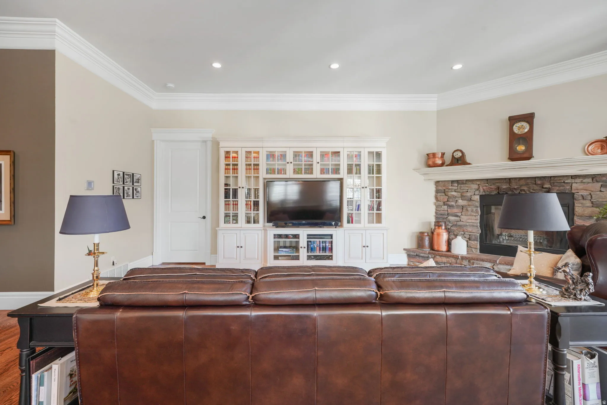 Living room featuring crown molding, dark wood-style flooring, a stone fireplace, and recessed lighting