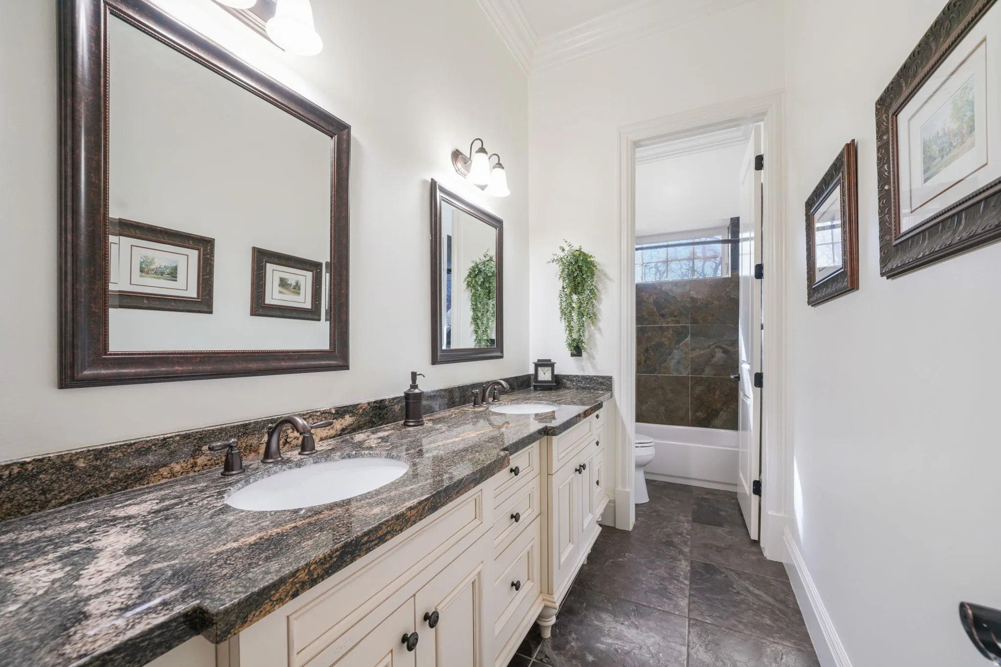 Bathroom with double vanity, crown molding, shower / bath combination, and dark stone finish floors