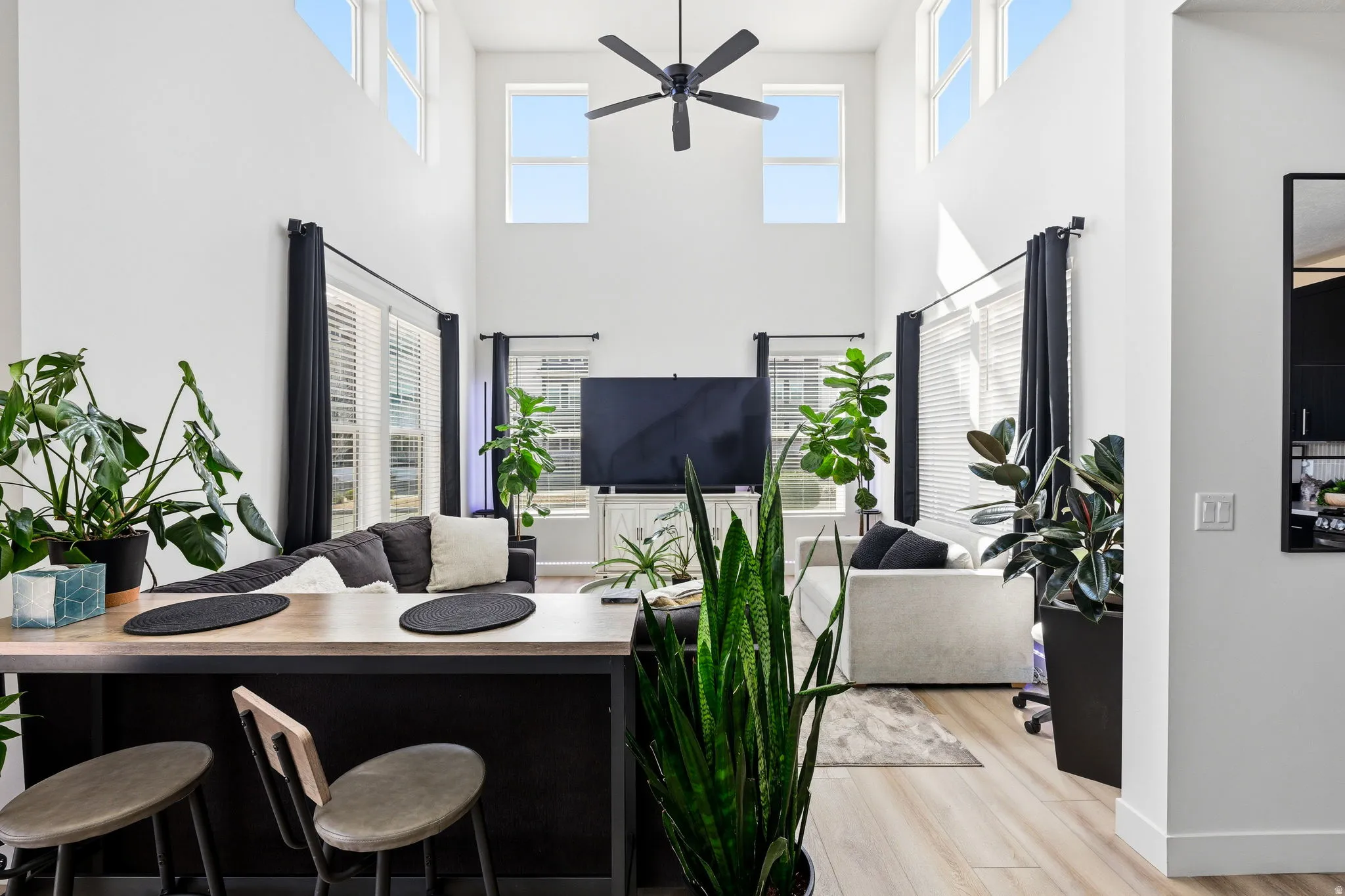 Living room with light wood finished floors, ceiling fan, plenty of natural light, and a high ceiling