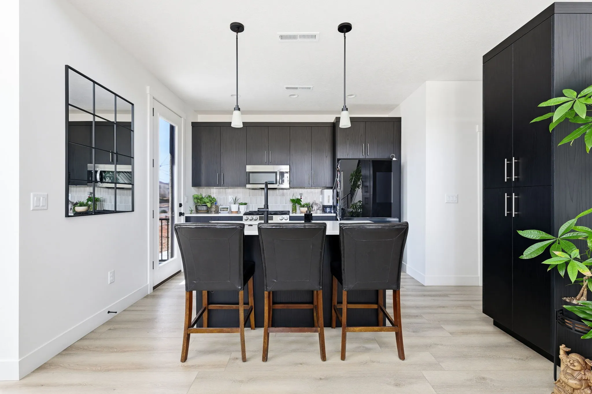 Kitchen featuring dark cabinetry, a center island with sink, decorative light fixtures, a kitchen breakfast bar, and stainless steel appliances