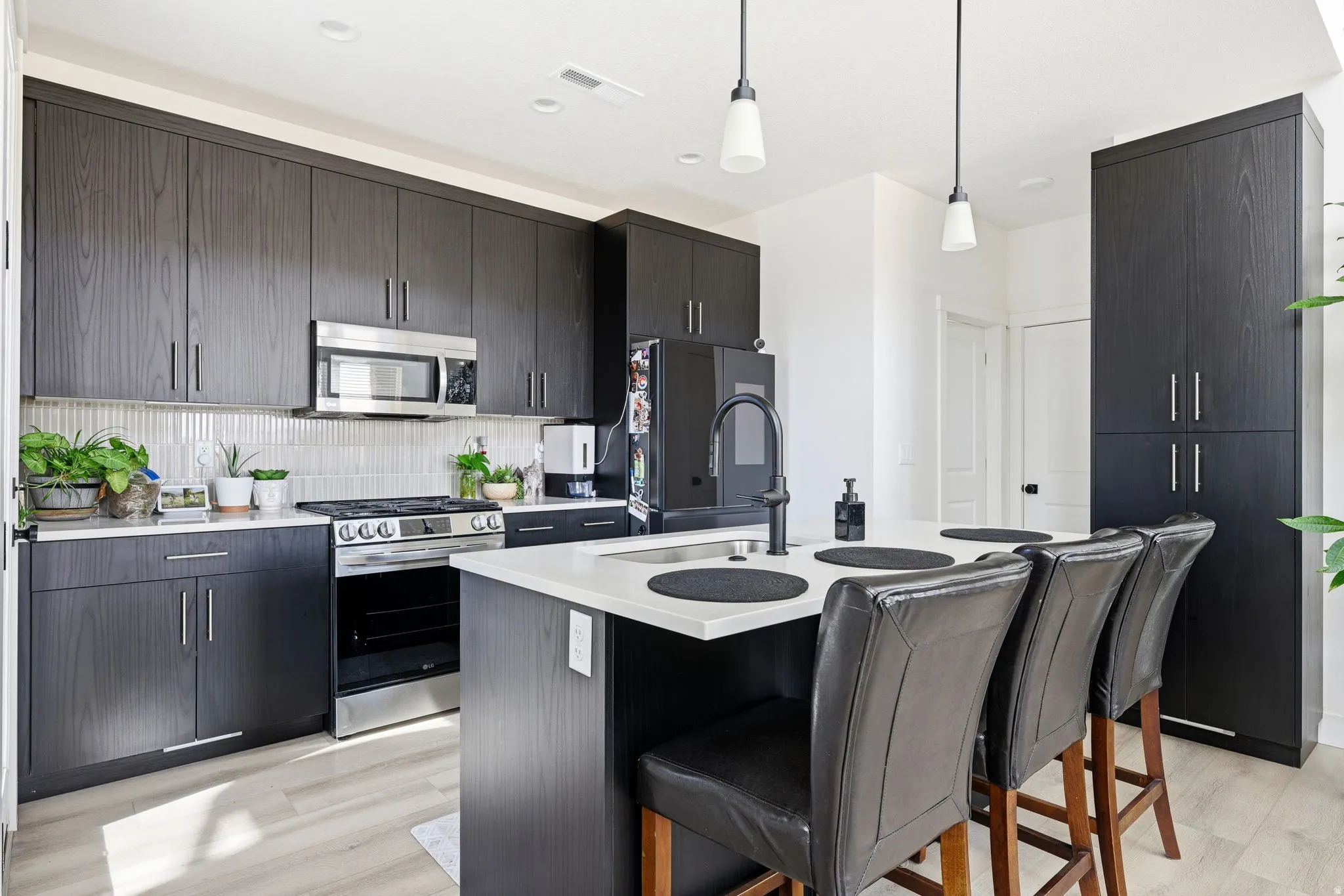 Kitchen featuring stainless steel appliances, tasteful backsplash, a center island with sink, a breakfast bar, and pendant lighting