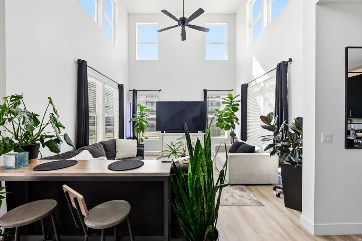 Living room with light wood finished floors, ceiling fan, plenty of natural light, and a high ceiling