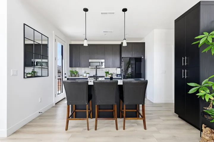 Kitchen featuring dark cabinetry, a center island with sink, decorative light fixtures, a kitchen breakfast bar, and stainless steel appliances