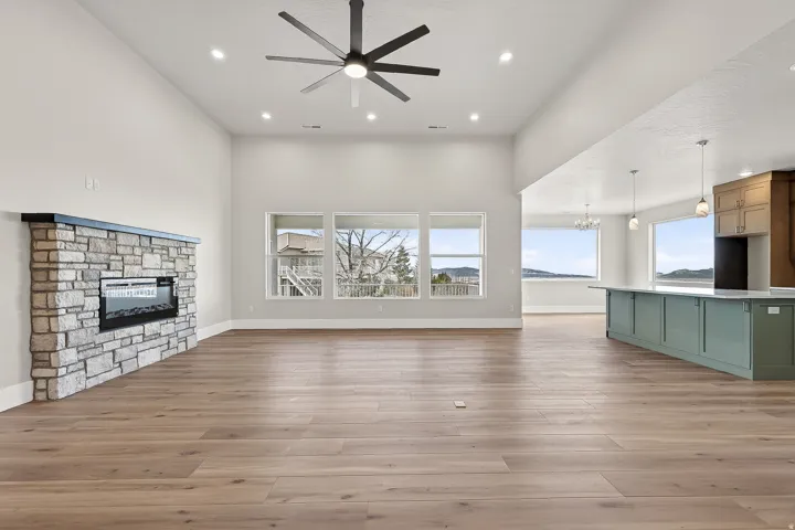 Unfurnished living room featuring ceiling fan, a stone fireplace, light wood-style flooring, a high ceiling, and suspended lighting