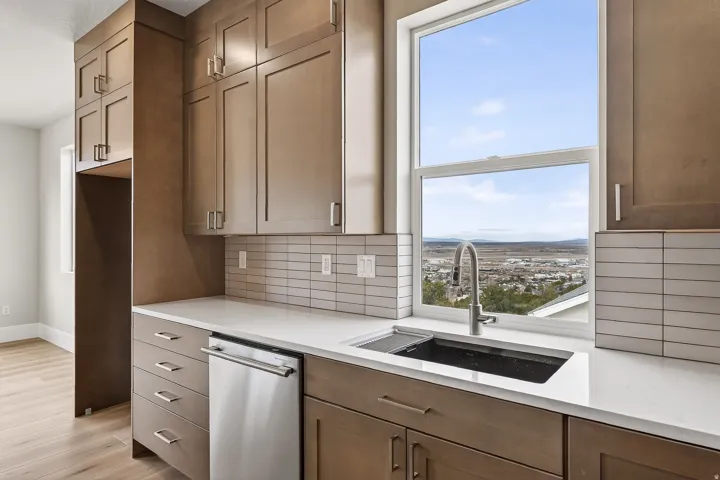 Kitchen featuring stainless steel dishwasher, light stone counters, light wood finished floors, and backsplash