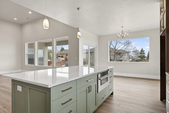 Kitchen with a kitchen island, light wood-style floors, hanging lights, light stone counters, and green cabinetry