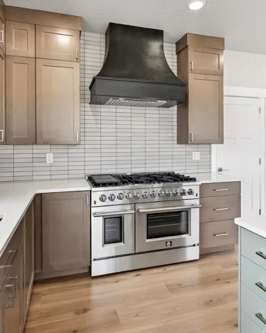 Kitchen with double oven range, tasteful backsplash, light wood-style floors, and light stone countertops