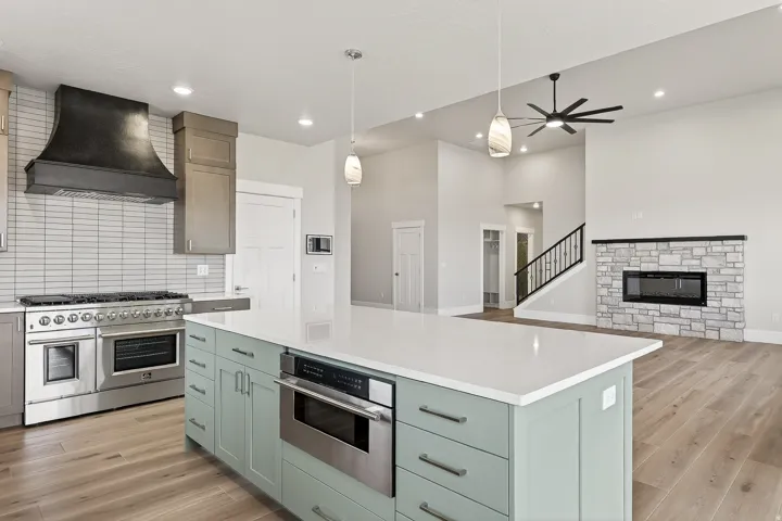 Kitchen featuring stainless steel appliances, light wood finished floors, ceiling fan, a fireplace, and a high ceiling